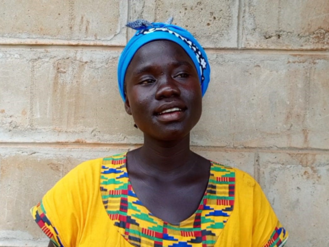 Winny, a young black woman wears a blue headscarf and a bright yellow top