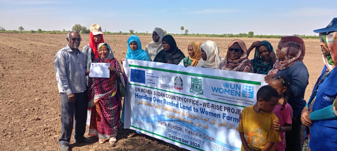 Women farmers and project participants stand with a donor banner, highlighting the collaboration between UN Women, Kassala University, and WOD, funded by the European Union, to strengthen women’s economic empowerment. (Photo: Courtesy of WOD)